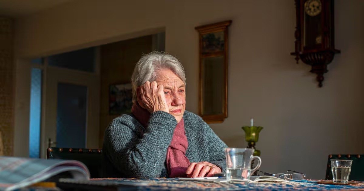 An older woman sitting at her kitchen table, resting her head on her hand while looking over paperwork